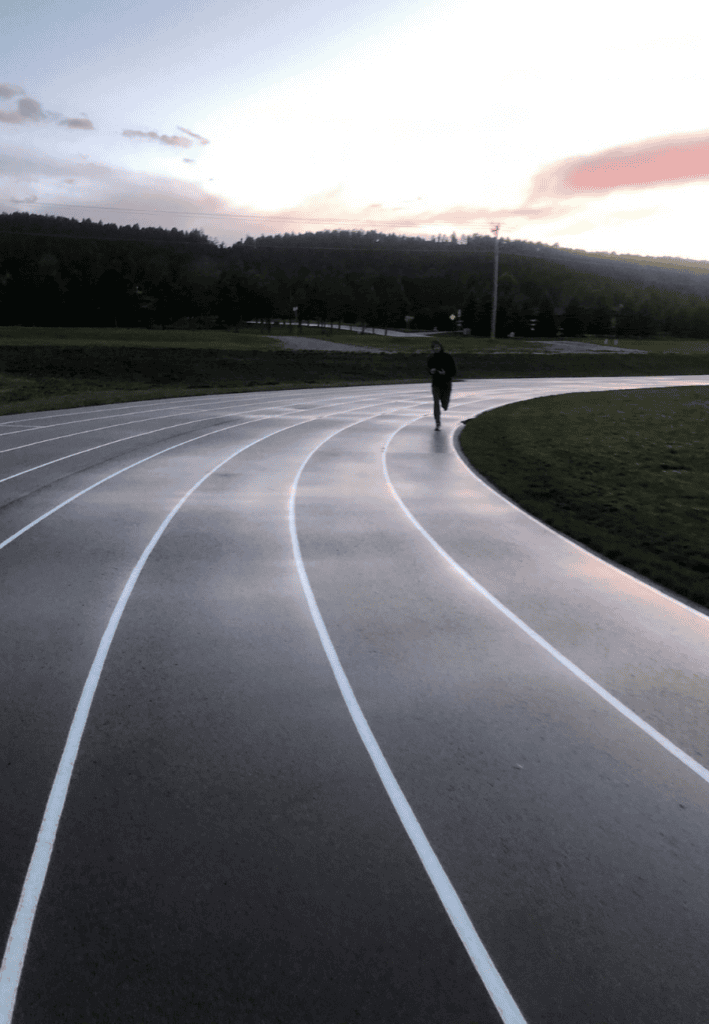 A wet asphalt athletic running track showcasing civil engineering geometric lane layout design, painted white alignment markings, and structural cross-slope drainage.
